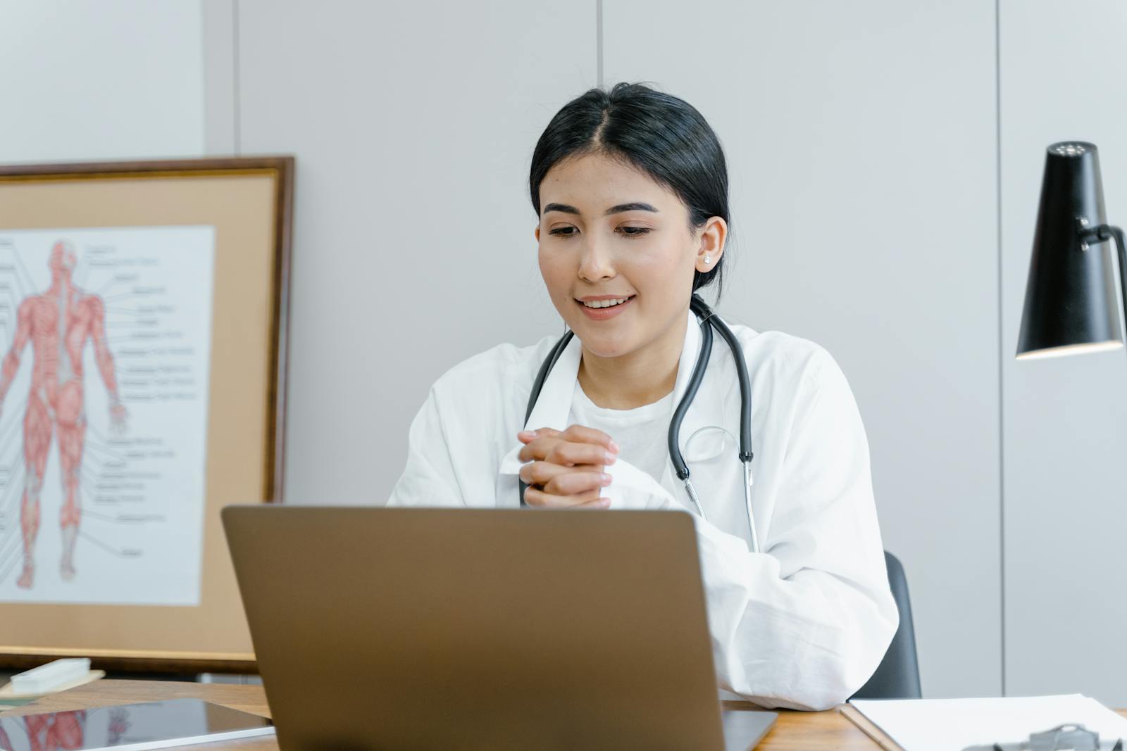 A young female doctor smiling while engaging in a telemedicine session on her laptop.